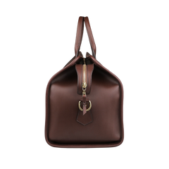 The Frank Clegg Chocolate Harness Belting Leather Signature Duffle features handcrafted quality with two handles, a zipper closure, and a decorative metal buckle on the front.