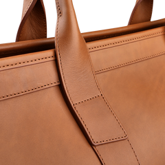 Close-up of the Frank Clegg Cognac Harness Belting Leather Signature Duffle highlighting its hand-crafted quality, with a focus on the handle and intricate stitching details made from premium leather.