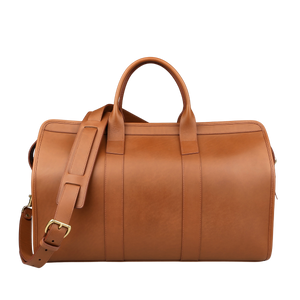 The Frank Clegg Cognac Harness Belting Leather Signature Duffle, featuring a shoulder strap and two handles, is displayed against a neutral background. This luxury travel bag epitomizes handcrafted quality and timeless elegance.