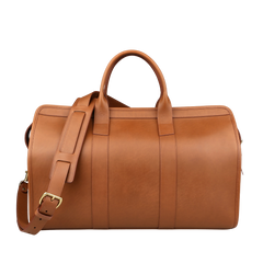 The Frank Clegg Cognac Harness Belting Leather Signature Duffle, featuring a shoulder strap and two handles, is displayed against a neutral background. This luxury travel bag epitomizes handcrafted quality and timeless elegance.