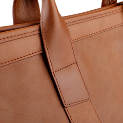 A close-up of Frank Clegg's Cognac Tumbled Leather Signature Duffle emphasizes its luxurious, hand-crafted quality with a focus on the handle and intricate stitching details.