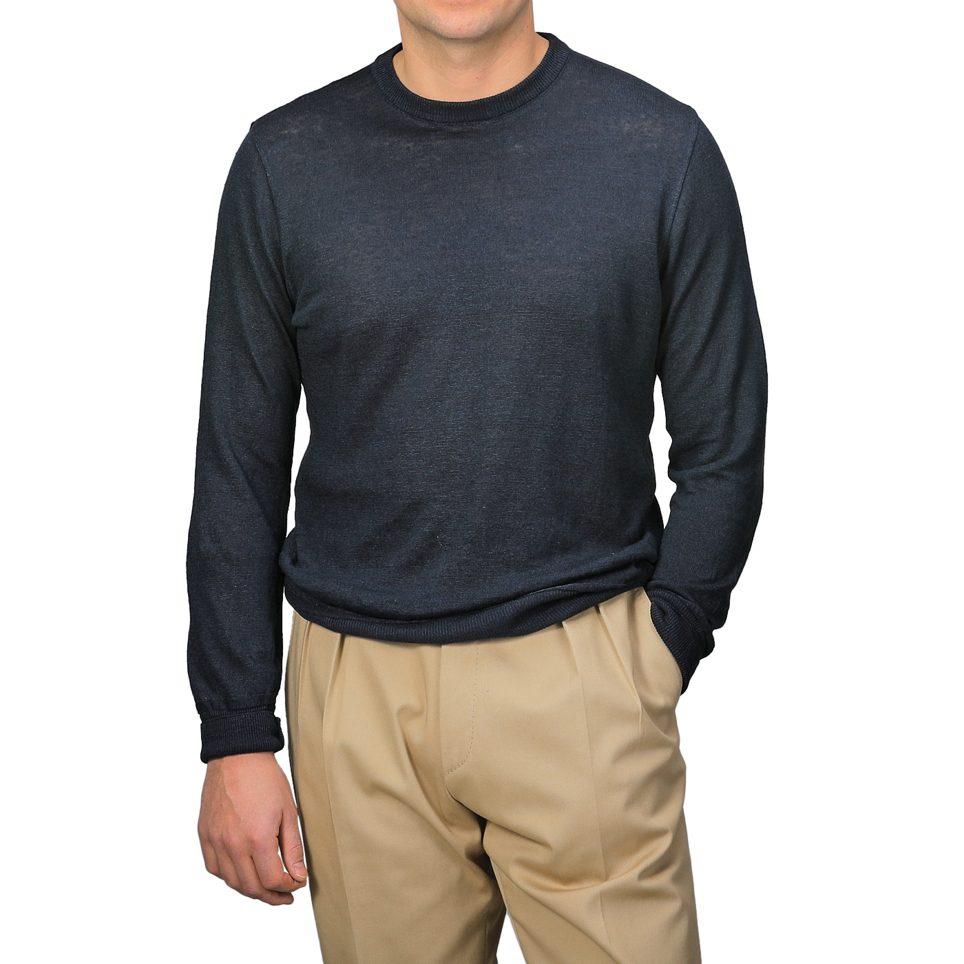 A person wears a G.R.P Dark Blue Linen Crewneck Sweater with lightweight beige pants and stands against a light gray background, one hand in their pocket.