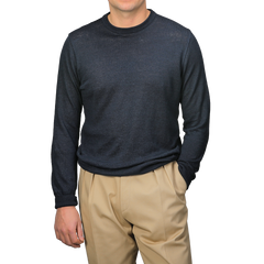 A person wears a G.R.P Dark Blue Linen Crewneck Sweater with lightweight beige pants and stands against a light gray background, one hand in their pocket.