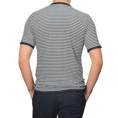 Individual in a Blue Ecru Striped Linen Henley T-Shirt by G.R.P and dark pants, viewed from the back, stands against a plain gray background.