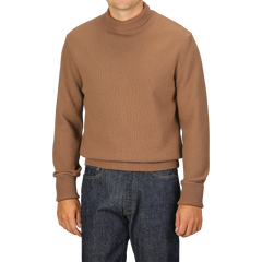 A person wearing a Camel Beige Wool Cashmere Mock Neck Sweater by G.R.P and dark blue jeans, standing against a plain background.