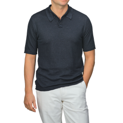 A man poses with one hand in his pocket against a plain background, wearing a dark blue linen polo shirt by G.R.P paired with light-colored pants.