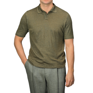 A person in a G.R.P Military Green Linen Polo Shirt and gray slim fit pants stands with one hand in their pocket, their face not visible.