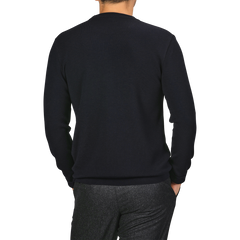 A person is standing with their back to the camera, wearing a Night Blue Wool Crewneck Sweater from G.R.P and gray pants.