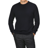 A person stands with hands in pockets, wearing a plain black long-sleeve shirt and gray trousers. Their head is not visible, but the outfit could be complemented perfectly with the night blue wool crewneck sweater from G.R.P for added elegance.