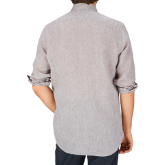 Back view of a person wearing a light gray Glanshirt Brown Melange Linen Regular Shirt with sleeves rolled up. The summer shirt adds to the relaxed vibe as the person stands with their arms by their sides.