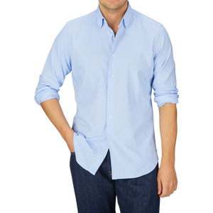Man wearing a Glanshirt Light Blue Cotton Oxford Regular Shirt with mother-of-pearl buttons and jeans against a grey background.
