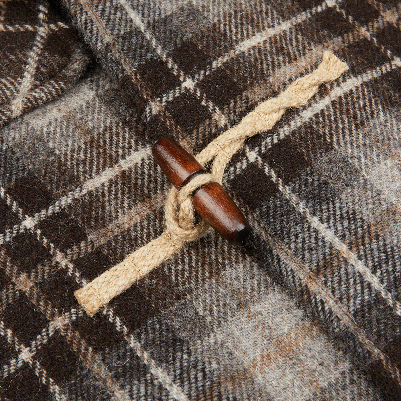 A close up of a Brown Undyed Shepherds Check Wool Duffle Coat by De Bonne Facture, with a wooden tassel, featuring collaboration and wool.