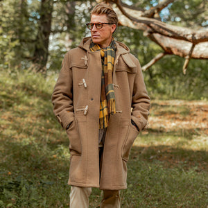 A man in a Gloverall Camel Wool Monty Duffel Coat standing in the woods.