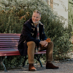 A man wearing a Gloverall Navy Blue Wool Union Jack Monty Duffle sits on a bench.