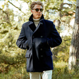 A man in a Gloverall Navy Wool Churchill Peacoat standing in a wooded area.