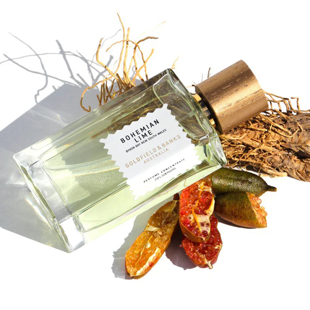 A 100ml bottle of Bohemian Lime Eau De Parfum by Goldfield & Banks rests on dried branches and colorful citrus peels, with hints of sandalwood weaving through its vibrant scent.