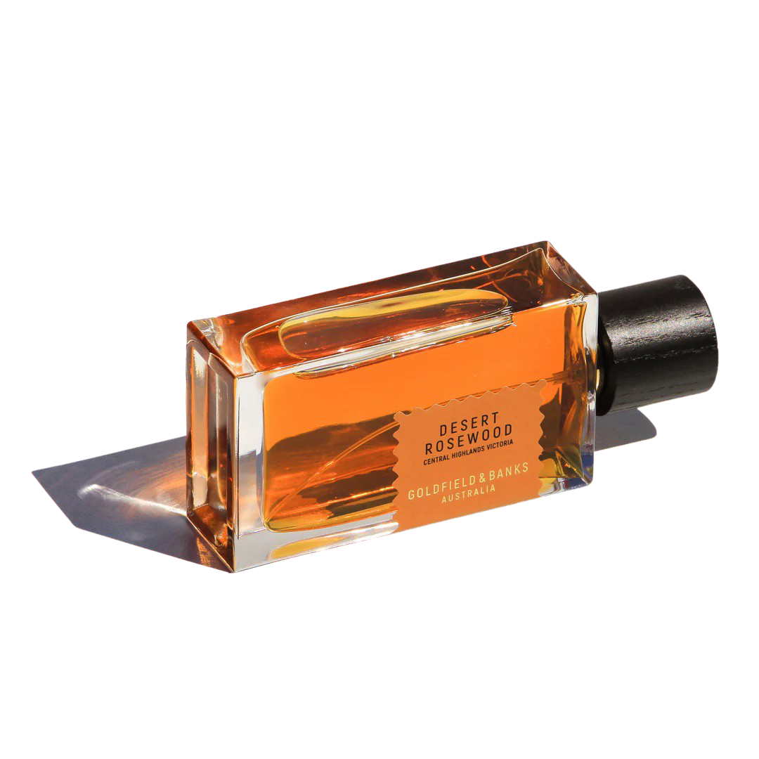 The Desert Rosewood 100ml Eau de Parfum by Goldfield & Banks is presented in a sleek rectangular glass bottle, showcasing its exotic blend with an amber-hued liquid and a sophisticated black cap, displayed elegantly against a white background.