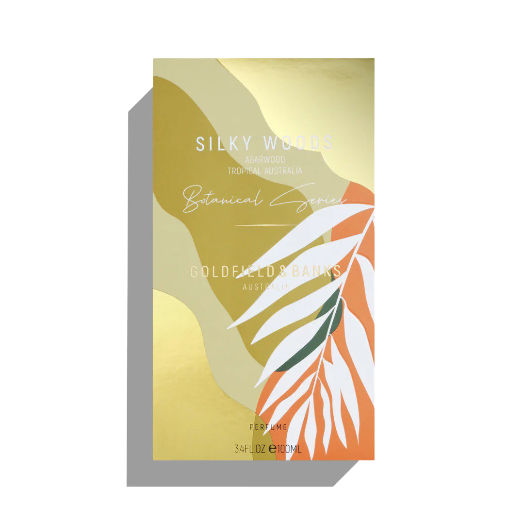 This luxury fragrance box features a gold and orange leaf design with "Silky Woods, Agarwood, Tropical Australia" prominently displayed. It is part of the Botanical Series by Goldfield & Banks and contains 100ml of exquisite Silky Woods Eau De Parfum.