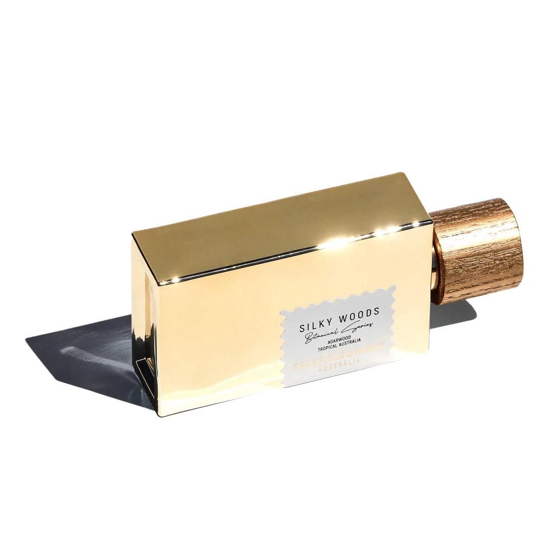 The Silky Woods 100ml Eau De Parfum by Goldfield & Banks is a luxurious fragrance housed in a gold rectangular bottle with an elegant wooden cap. The white and gold label gracefully showcases the name, embodying the essence and charm of refined sophistication.