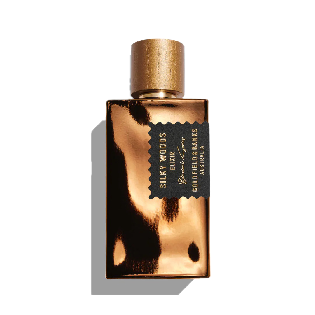 A gold perfume bottle labeled "Silky Woods Elixir 100ml Extrait de Parfum" by Goldfield & Banks, infused with the essence of exotic botanicals and featuring a sleek black and gold cap.