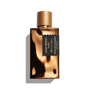 A gold perfume bottle labeled "Silky Woods Elixir 100ml Extrait de Parfum" by Goldfield & Banks, infused with the essence of exotic botanicals and featuring a sleek black and gold cap.