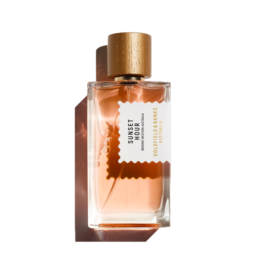 A bottle of Goldfield & Banks Sunset Hour 100ml Eau De Parfum features a gold cap and a peach-colored liquid inside, offering an exquisite blend of spicy notes with subtle floral hints for a unique olfactory experience.