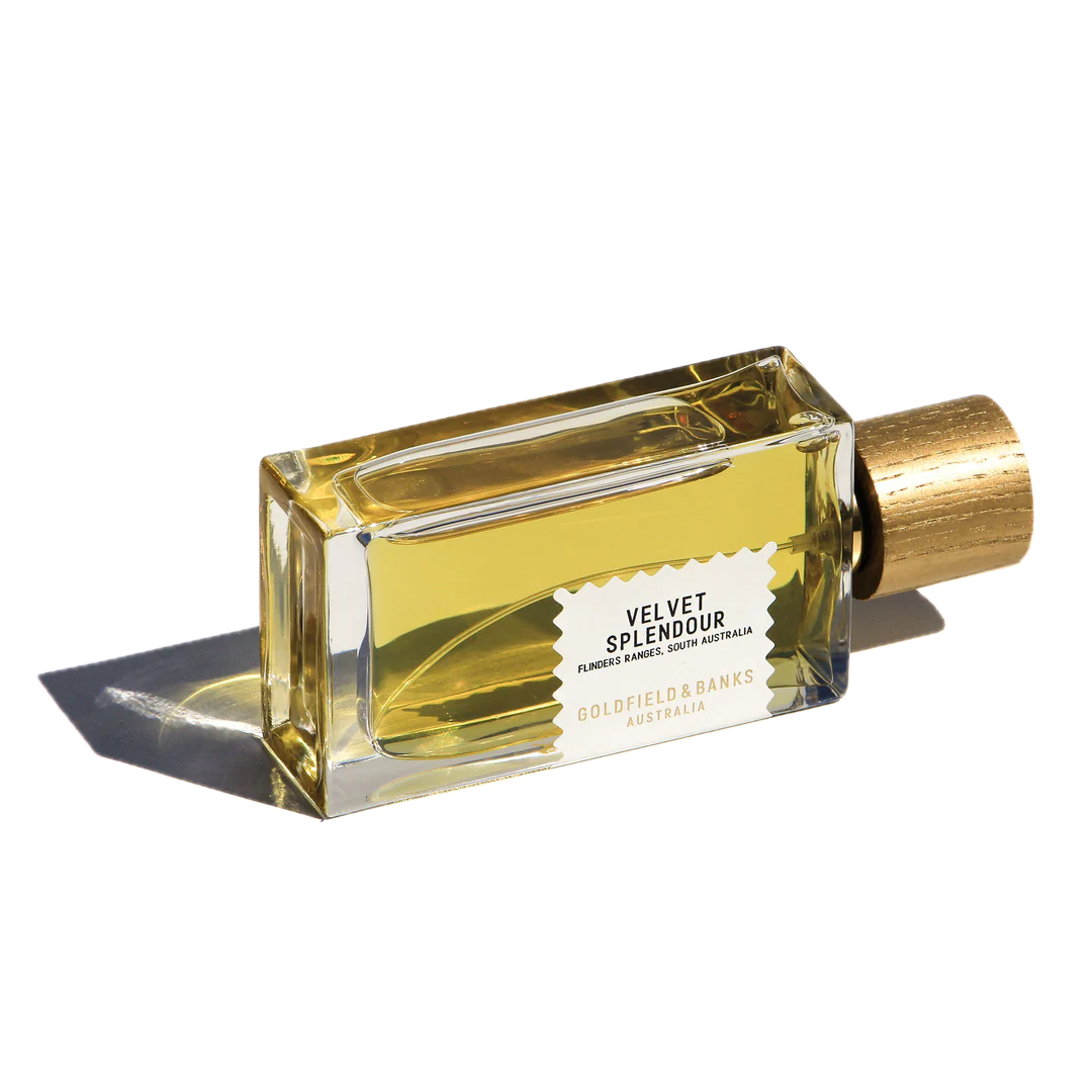 A rectangular bottle of Goldfield & Banks' Velvet Splendour 100ml EdP, inspired by wildflowers, featuring a wooden cap, cast shadows on a plain backdrop.