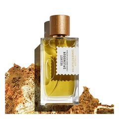 A 100ml bottle of Velvet Splendour Eau de Parfum by Goldfield & Banks, featuring a wooden cap, is set against a textured, earthy background. Its scent captures the essence of wildflowers blooming beneath the shade of a mimosa tree.