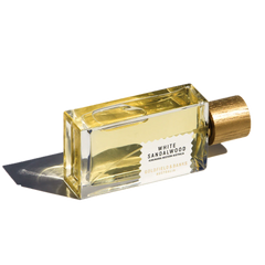 A 100ml bottle of Goldfield & Banks White Sandalwood Eau De Parfum, infused with hints of amber and adorned with a golden cap, rests elegantly on its side, casting a graceful shadow.