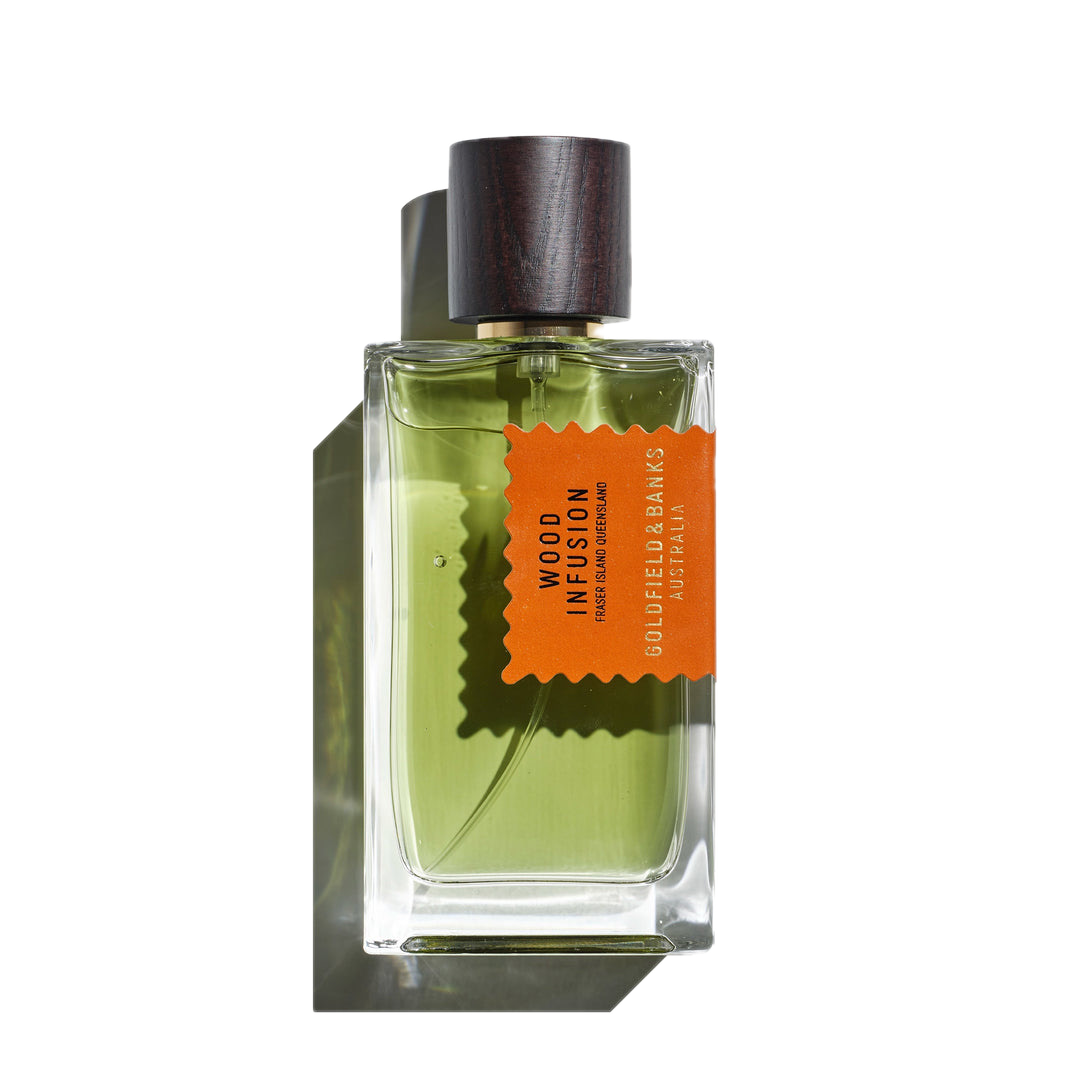 The green perfume, encased in a clear glass bottle and topped with a dark wood cap, displays an orange label reading "Wood Infusion, Goldfield & Banks, Australia." This fragrance weaves together a rich tapestry of Australian woods with subtle notes of rare Sandalwood Album.