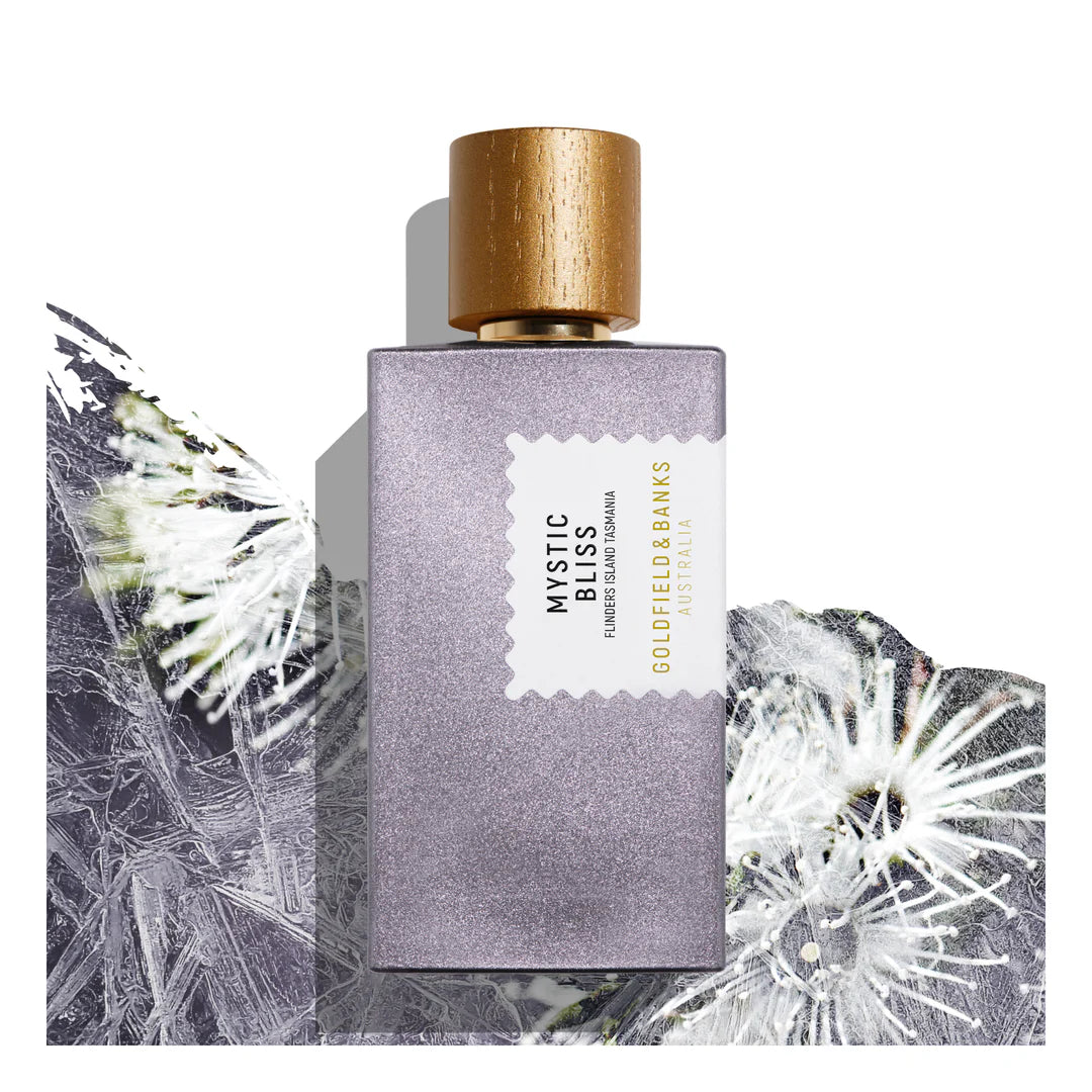 The Goldfield & Banks Mystic Bliss 100ml Eau De Parfum, housed in a rectangular bottle topped with a gold cap, exudes elegance against a textured floral background, hinting at the warm allure of cedarwood.