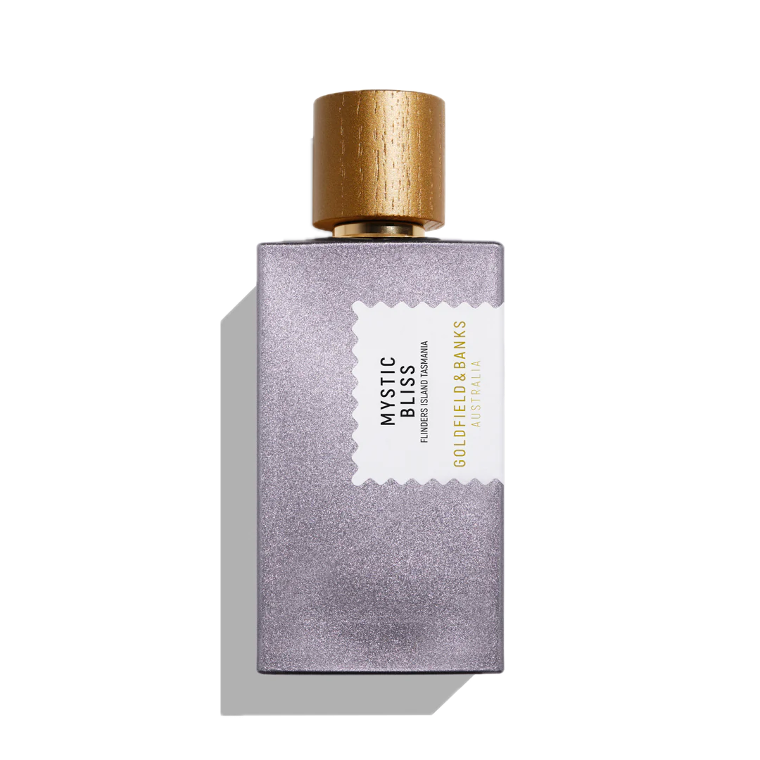 A 100ml bottle of Mystic Bliss Eau De Parfum by Goldfield & Banks, with notes of cedarwood, features a textured purple body and a gold cap, all set gracefully against a white background.