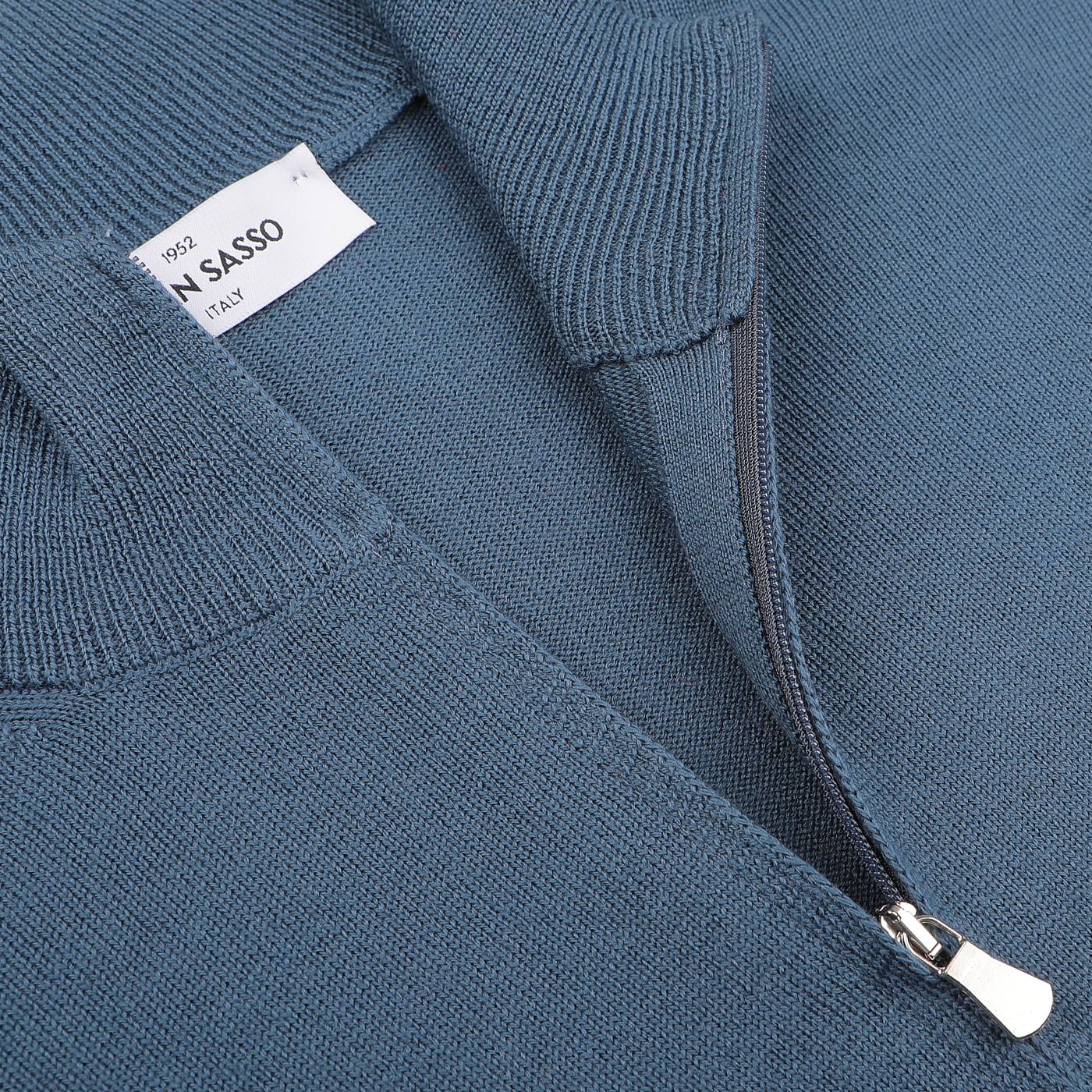 Close-up of a zip cardigan, airforce blue in color and crafted from extrafine merino wool, with a partially open zipper revealing a label that reads "Gran Sasso" and "Italy.