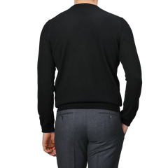 A person is wearing a black cashmere crewneck sweater by Gran Sasso and gray pants, viewed from behind.