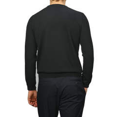 A person is seen from behind, dressed in Gran Sasso's Black Extra Fine Merino Crew Neck and black pants, standing out against a neutral background with classic allure and understated elegance.