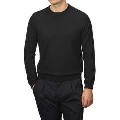 A person in Gran Sasso's Black Extra Fine Merino Crew Neck and dark pants stands against a gray background, displaying a sophisticated wardrobe choice.