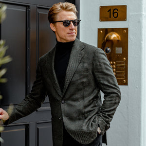 A man in a Gran Sasso Black Extra Fine Merino Roll Neck suit leaning against a door.