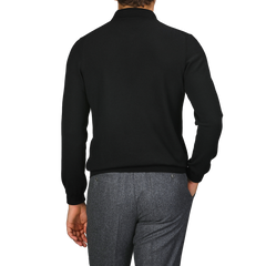 A person wearing a black long-sleeve shirt, likely the Black Extra Fine Merino Wool Polo Shirt by Gran Sasso, and gray pants is shown from the back against a neutral background.