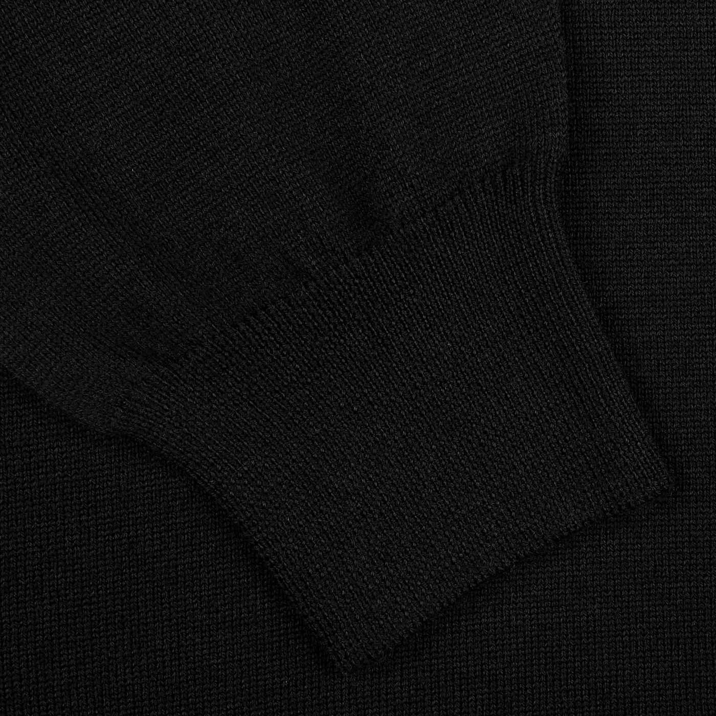 Close-up of a black polo shirt's cuff, highlighting the intricate knit texture of luxurious extra fine merino wool by Gran Sasso.