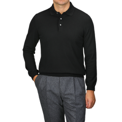 A person wearing a Gran Sasso Black Extra Fine Merino Wool Polo Shirt and gray trousers stands with one hand in their pocket against a neutral background.