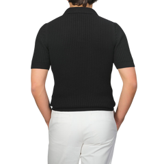 Person wearing a Gran Sasso black organic cotton polo shirt paired with white pants, facing away.