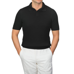 A person is wearing a Gran Sasso Black Organic Cotton Polo Shirt, slim fit style, paired with white pants and hands in pockets.