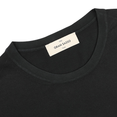 Close-up of a black organic cotton T-shirt with a beige "Gran Sasso, Made in Italy" label inside the collar, offering a stylish and sustainable choice.