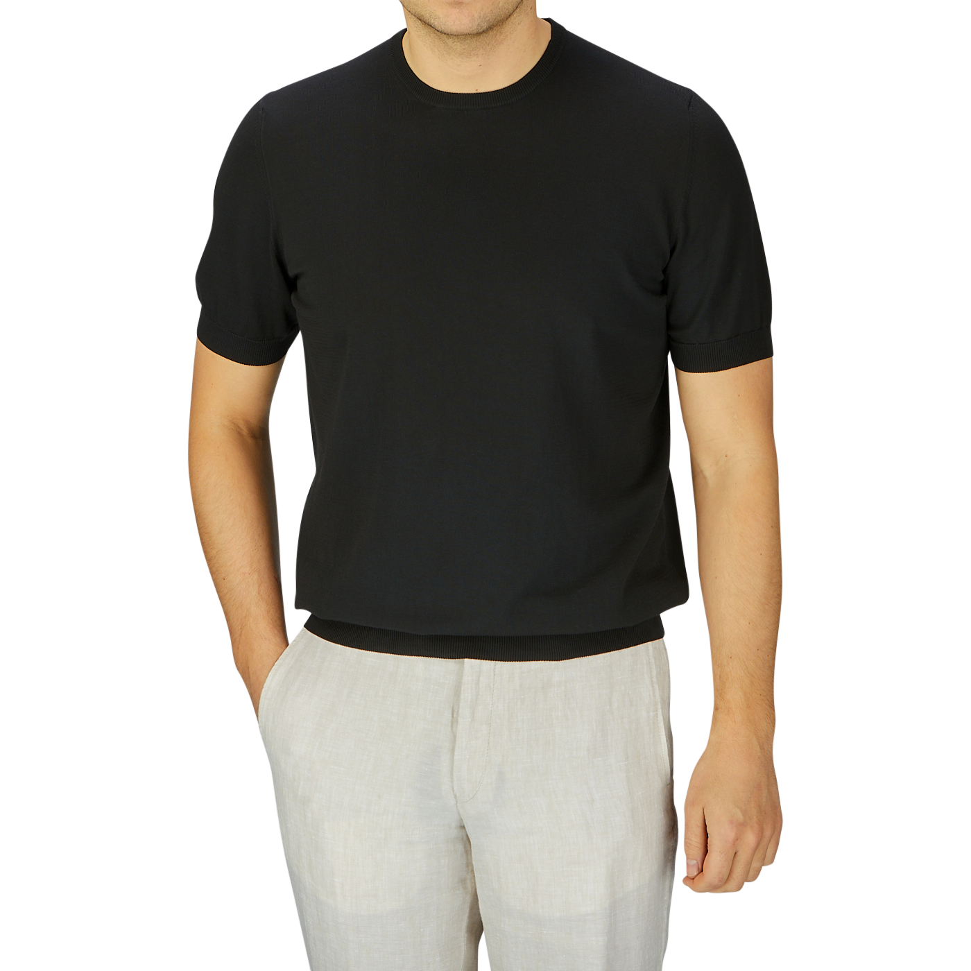 Man wearing a Gran Sasso black organic cotton t-shirt and light beige pants, standing against a grey background, cropped at neck.