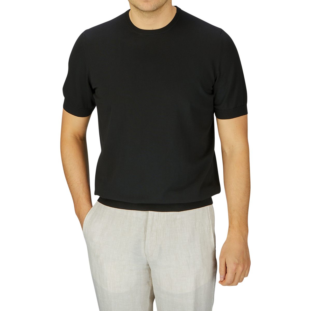 Man wearing a Gran Sasso black organic cotton t-shirt and light beige pants, standing against a grey background, cropped at neck.