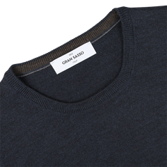 Close-up of a Blue Melange Extra Fine Merino Crew Neck sweater with a white label reading "Gran Sasso" on the collar. The collar edge also features a brown trim, adding an extra layer of warmth.