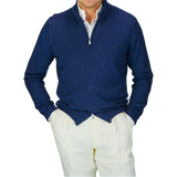 Man in a Blue Melange Vintage Merino Wool Zip Cardigan by Gran Sasso and white pants, exuding a vintage feel.