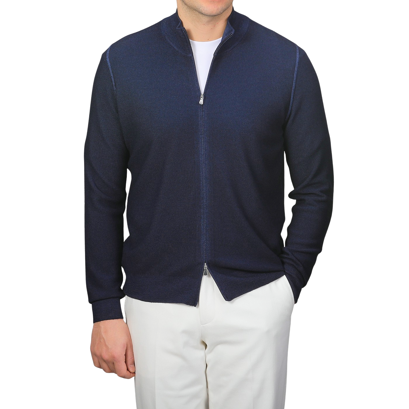 A man wears a Blue Melange Vintage Wool Zip Cardigan by Gran Sasso with white pants, hands in pockets, exuding a vintage feel.