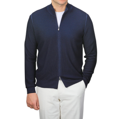 A man wears a Blue Melange Vintage Wool Zip Cardigan by Gran Sasso with white pants, hands in pockets, exuding a vintage feel.