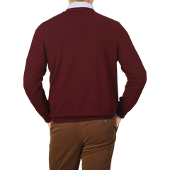 Man in brown pants and a Gran Sasso Bordeaux Extra Fine Merino Wool Cardigan, facing away from the camera, holding his hands behind his back against a plain background. The pure merino wool and mother of pearl buttons add subtle elegance to his attire.